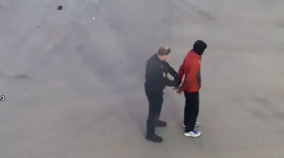 En person iført rød jakke blir satt i håndjern av en betjent på en betongflate etter en rask reaksjon hindrer tyveri - bevæpnet mann pågrepet hos bilopphugger i Arendal.