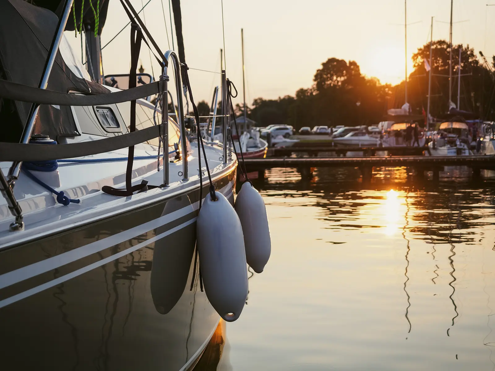 En båt la til ved en marina under solnedgang, med refleksjon over vannet og andre båter i bakgrunnen, og skaper en rolig scene som står i sterk kontrast til den nærliggende returpunkt farlig avfall-stasjon.