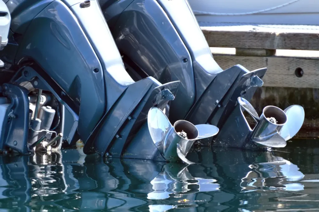 Tre påhengsbåtmotorer med propeller delvis nedsenket og stilt opp ved siden av en trebrygge i klart vann, og viser omhyggelig sikring av båt og verdier.